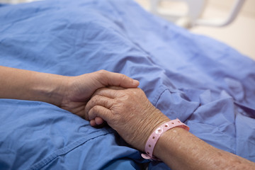 The hand of the woman is holding mother's hand that sleeping in the hospital bed