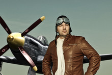 Portrait Of A Vintage Pilot With Leather Cap, Scarf And Aviator Glasses In Front Of A Historic Airplane - Portrait Of A Man In Historical Pilot Clothing