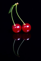 Symmetric reflection of red sour cherry on a black reflective surface