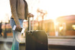 © terovesalainen - Train station at sunset. Woman standing in platform waiting and holding ticket and passport in hand. Person with suitcase and luggage.