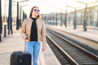 © terovesalainen - Woman waiting for train at station. Happy smiling lady at platform going on railway trip. Person holding passport and ticket and looking at the tracks.