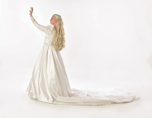 full length portrait of blonde woman wearing long white bridal gown. standing pose on white studio background.