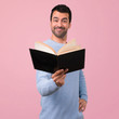 © luismolinero - Man with blue sweater holding and reading a book on pink background