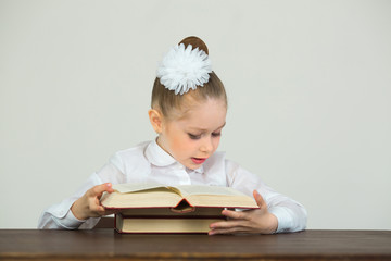 Wall Mural - beautiful young girl with a bow sitting reading book on a gray background