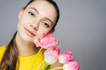 cute young girl in a yellow dress holding a bouquet of pink flowers, smiling and looking at the camera