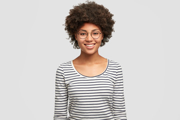 Wall Mural - Positive emotions concept. Happy young smiling African American female in spectacles, rejoices unforgettable party with friend, dressed in casual striped jacket, isolated on white background