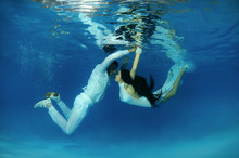 Bride And Groom In A White Wedding Dress Swim To Each Other Underwater In The Pool. Underwater Wedding