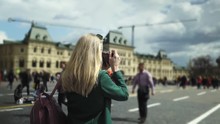 Rear View Of A Blonde Young Tourist Wearing A Green Coat Making Photos Of Saint Basil's Cathedral. Moscow, Russia. Sunny Day. Blurred Background. Slider Real Time Medium Shot.
