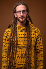 Young handsome Hispanic man with dreadlocks against brown backgr