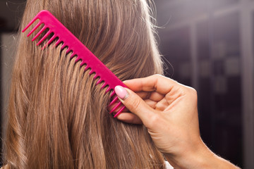 Wall Mural - close up process of brushing hair of a young model. professional hairdresser using a pink brush in a beauty salon. concept of carefull hair treating