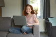 © Joerch - Hübsche rothaarige Frau mit einem Laptop sitzt auf einer Couch und lacht