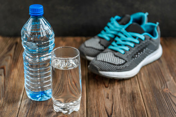 Wall Mural - Bottle and glass of water and sneakers on wooden background with copy space.