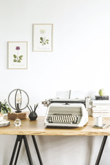 The stylish home office with vintage typewriter, poster illustrations of plants, table lamp, wooden desk and office accessories.