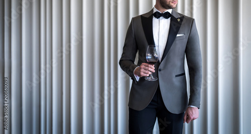 Valokuvatapetti Man in custom tailored tuxedo, suit holding glass with wine and posing indoors i
