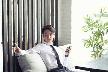 A young Asian businessman is waiting for a partner in a cafe. Bu