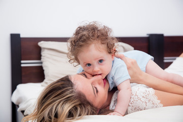 Wall Mural - Young mother with her 7 month old little son dressed in pajamas are relaxing and playing in the bed at the weekend together, lazy morning, warm and cozy scene.