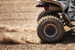 ATV quadbike start in a stony road and having wheel-spin making a spray of debris.