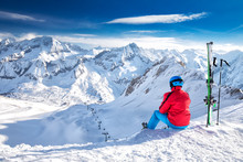 Young Happy Skier Sitting On The Top Of Mountains And Enjoying View Of Rhaetian Alps, Tonale Pass, Italy, Europe.
