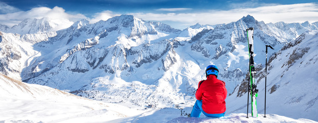 Young happy skier sitting on the top of mountains and enjoying view of Rhaetian Alps, Tonale pass, Italy, Europe