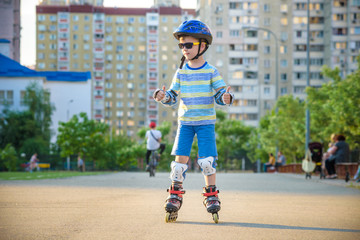 Wall Mural - Little boy riding on rollers in the summer in the Park. Happy child in helmet learning to skate