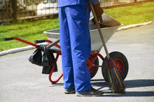 A Man In A Working Overall With A Whisk In His Hand And With A Garbage Cart. Summer Cleaning In The City. Close-up.