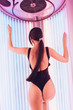 © mnelen.com - slim luxury girl brunette in a black bathing suit sunbathing in a vertical sunbed under the ultraviolet rays