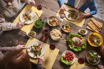 Top view of healthy food served for household members. They are sitting and eating together in kitchen vegetables, salads, meat and drinking wine