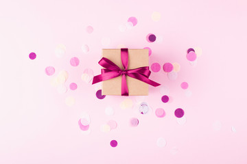 Wall Mural - Kraft gift box tied with pink bow on pink background decorated with confetti.. Top view, holiday present concept.