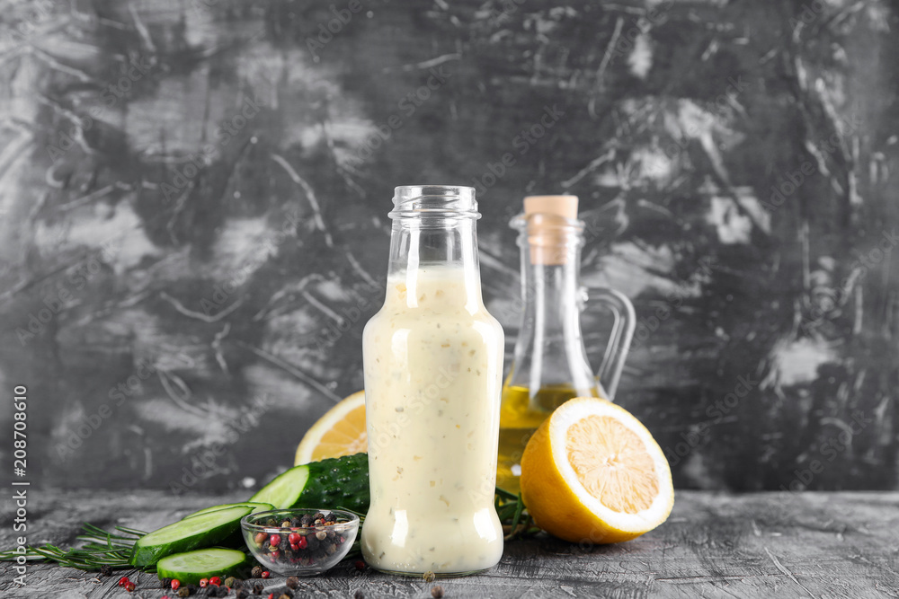 Bottle with tasty white sauce, cucumber and lemon slices on grey table