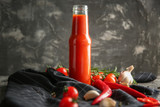Bottle with tasty tomato sauce and vegetables on table