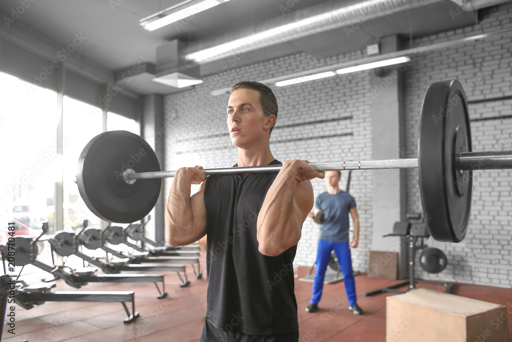 Athletic man training with barbell in modern gym