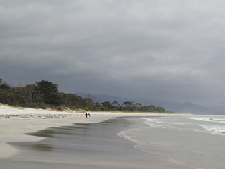 Pastell colored dramatic sky with two people walking at Bicheno Beach, Bay of Fires, Tasmania, Australia