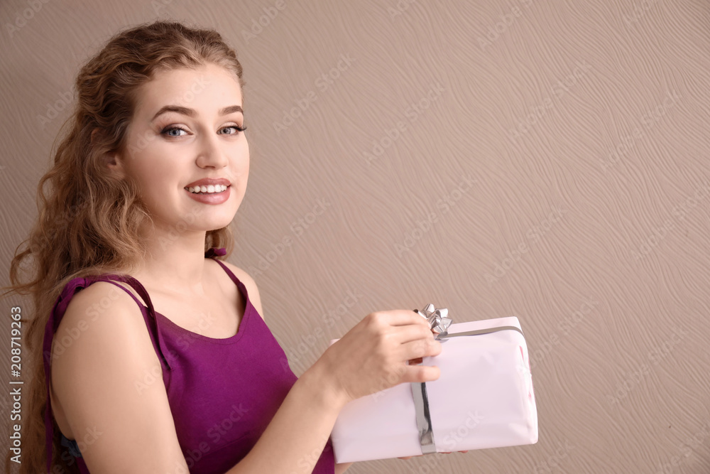 Beautiful young woman with gift box on color background