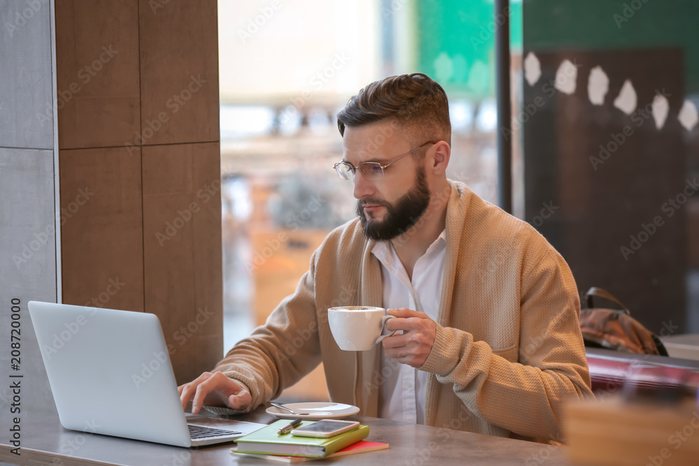 Young freelancer with cup of coffee and laptop working in cafe