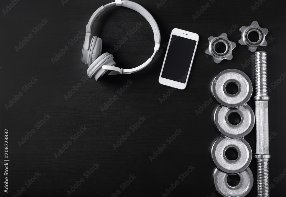 Flat lay composition with weight plates, smartphone and headphones on black background. Gym workout