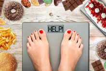 Diet Temptation Or Hard To Lose Weight Concept With Woman Weighing On Bathroom Scale With Many Sweets And Fast Food Around
