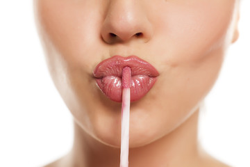 young beautiful woman apply a lip gloss on her lips on white background