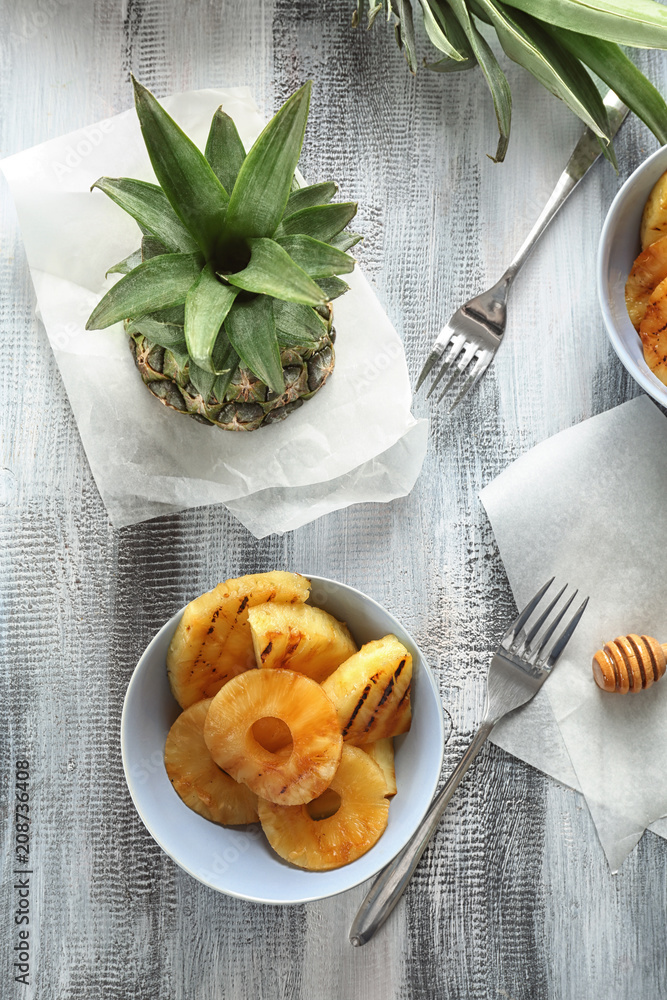 Bowl with grilled pineapple slices on wooden table