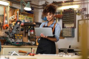 Wall Mural - 
Young woman using a laptop in a workshop
