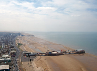 an aerial view of blackpool beach looking north showing the south and central piers at low tide with the main road and town stretching to the horizon on a bright summer day with blue sky and clouds