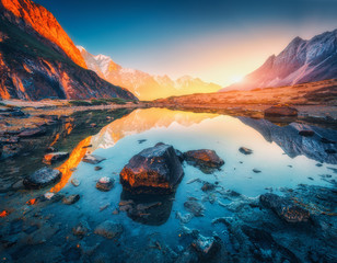 Wall Mural - Beautiful landscape with high mountains with illuminated peaks, stones in mountain lake, reflection, blue sky and yellow sunlight in sunrise. Nepal. Amazing scene with Himalayan mountains. Himalayas