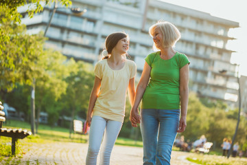 grandmother and granddaughter are walking in park in summer.