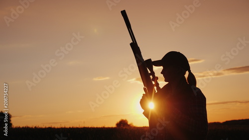 Fotografía Beautiful silhouette of a woman with a rifle in the rays of the setting sun