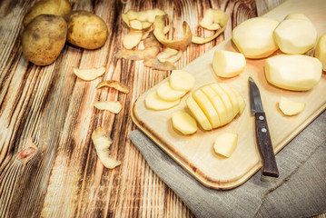 Raw peeled sliced potato, pile of potatoes and knife on rustic wooden table.