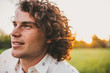 © Z A C - Handsome young freckled male smiling with white toothy smile and curly hair posing on the lawn in the park looking a side, sunset view. Copy space for your advertising. People, lifestyle and emotion