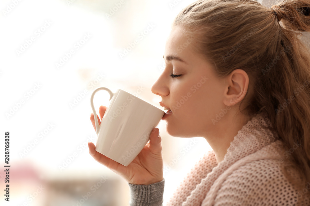 Young woman drinking tea on blurred background