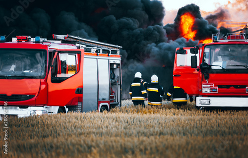Fotografía Red fire trucks in front of huge black smoke from the fire