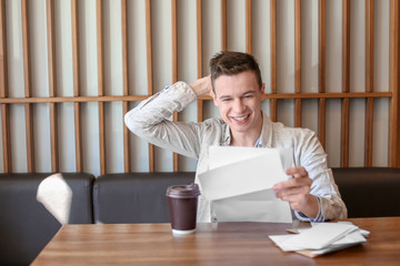 Canvas Print - Young man reading letter at table in cafe. Mail delivery