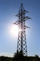 A post with high-voltage wires, against a background of blue sky and sun.