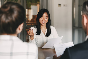 Wall Mural - Business, career and placement concept - businesslike asian woman holding resume and speaking to employers of big company, during corporate meeting or job interview